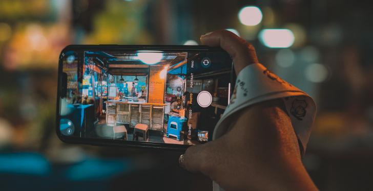 One hand is holding a smartphone with camera function that films a store...