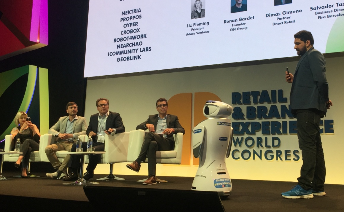 Five people on a stage in front of a big screen with a small humanoid robot;...