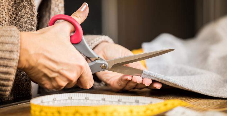 Tailor cutting fabric and measuring tape on the table; copyright:...