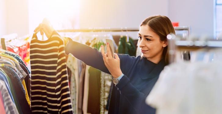 Woman looking at clothing in a store and taking a picture with her smartphone;...