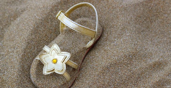 Sandal with a decorative flower half buried in sand; copyright: Bildagentur...