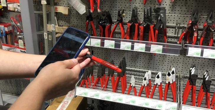 Person scans barcode on red pliers with a smartphone in a DIY market;...