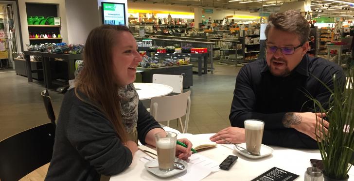 Left woman, right man - sitting at a table in the shop and talking....