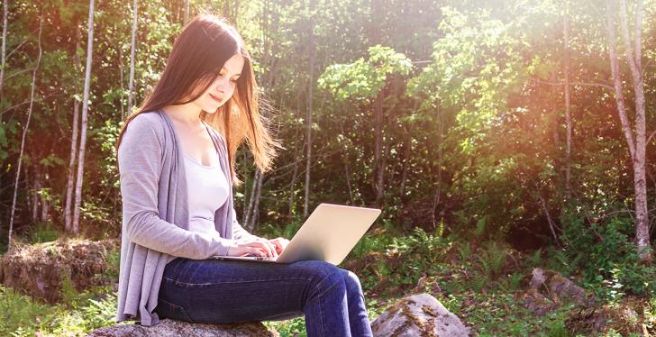 Young woman sitting on a rock, using a computer