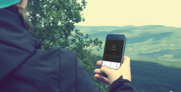 Person with view over wooded hills in outdoor clothing looks at smartphone...