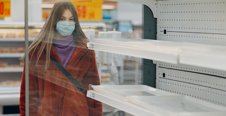 Woman with breathing mask stands in front of empty shelves in the supermarket...