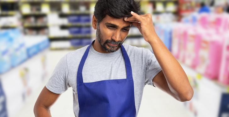 Ein männlicher Supermarktangestellter fasst sich mit der Hand an den Kopf...