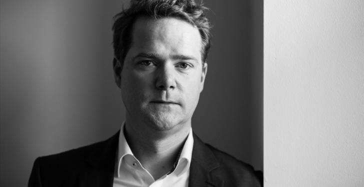 A young man in a suit looks into the camera