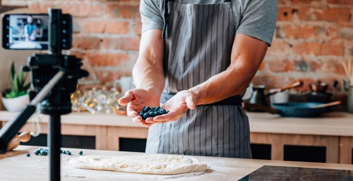 A man in a cooking apron shows a handful of berries to a camera...