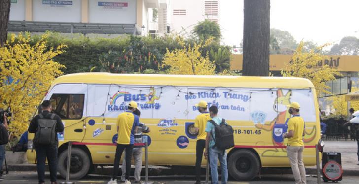 A yellow bus on a street and people standing around it; copyright: DONY Garment...