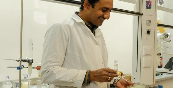 A scientist in a laboratory holding a Petri dish and a pipette...