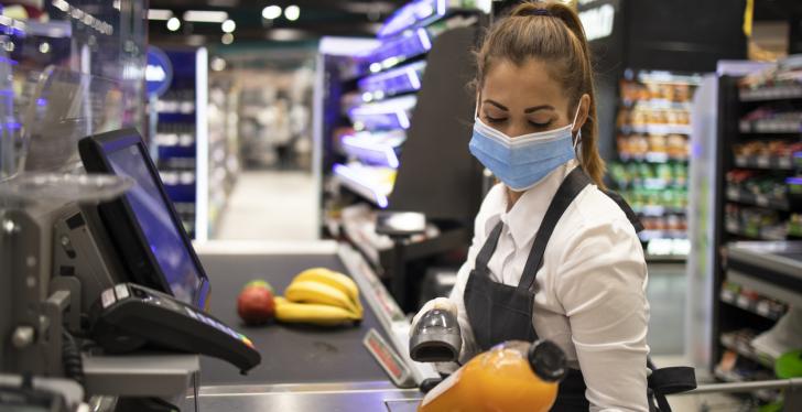 Cashier in supermarket wearing mask and gloves fully protected against corona...