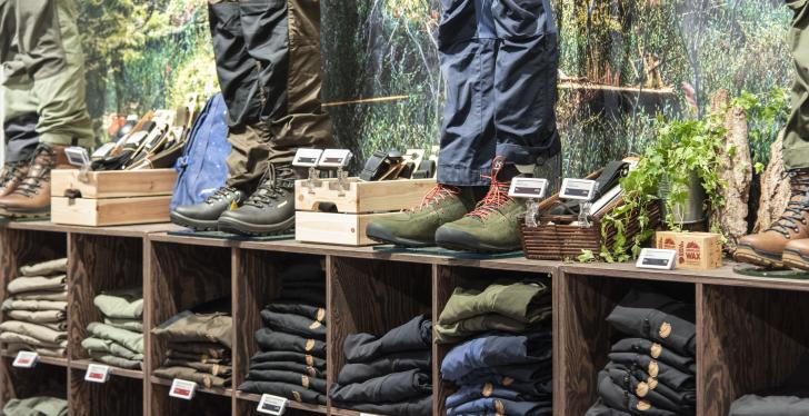 Shelf with pants and hiking boots, marked with digital price tags...