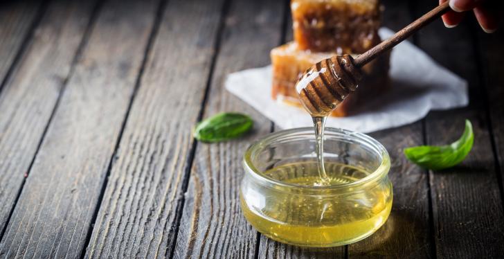 A honey spiral from which honey flows into a glass, behind it solid honey...