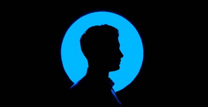 A black silhouette of a male head infront of a blue circle and a black...