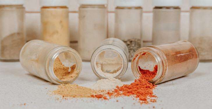 Three different spice powders fall from three jars onto a table; copyright:...
