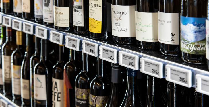 Various bottles of wine are placed on a shelf with electronic shelf labels....