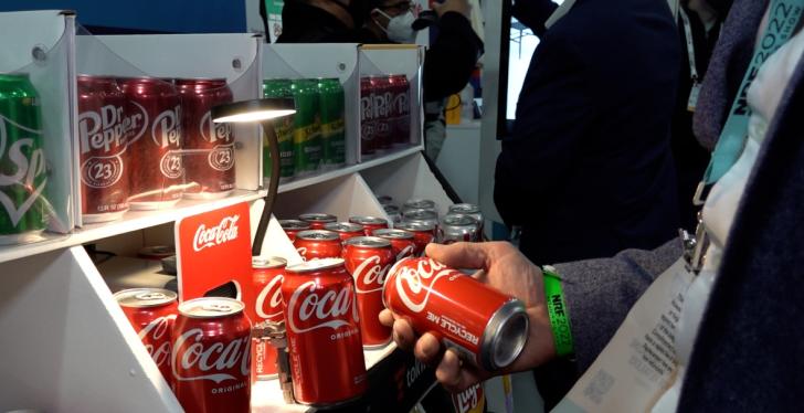 Someone picks a coke out of a shelf with many drink cans, a robotic arm is...