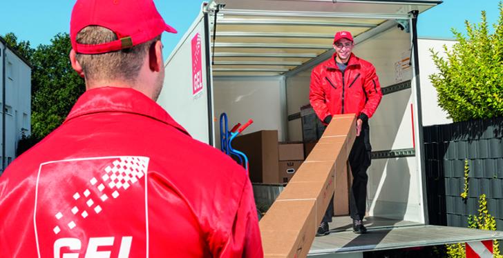 2 Männer in roten Anziehsachen laden Paket aus Transporter...