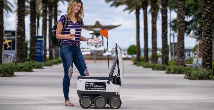A person takes a pizza and a drink from a self-driving robot...