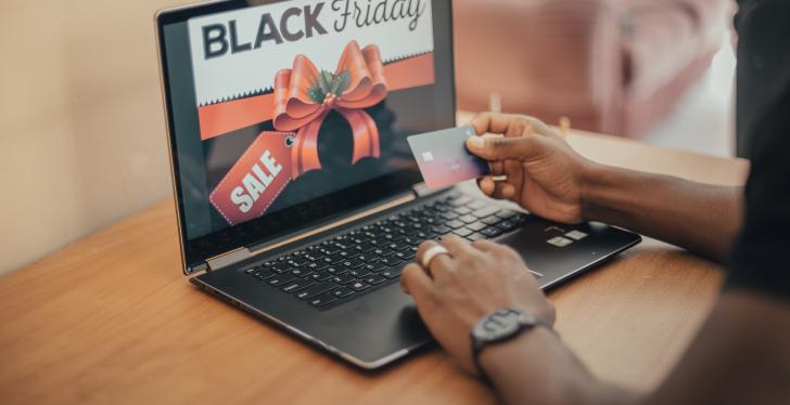 A person is sitting at a laptop. The laptop shows the Black Friday Sale....