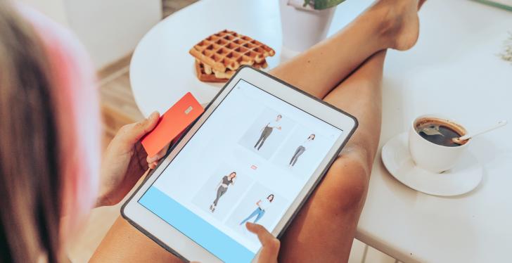 A woman shops online with a tablet while enjoying a coffee....