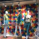 Three female mannequins in front of a wall of colored pinwheels in a shop window...