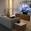 A gray sofa in front of a television, with “Lancia” written above it...