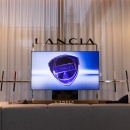 A gray sofa in front of a television, with “Lancia” written above it...