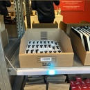 Carton with compact black articles on the shelf, blue pick-by-light indicates...