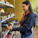 Person holds product and scanner, shopping cart is filled with selected items....