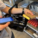 Person holds product and scanner, shopping cart is filled with selected items....
