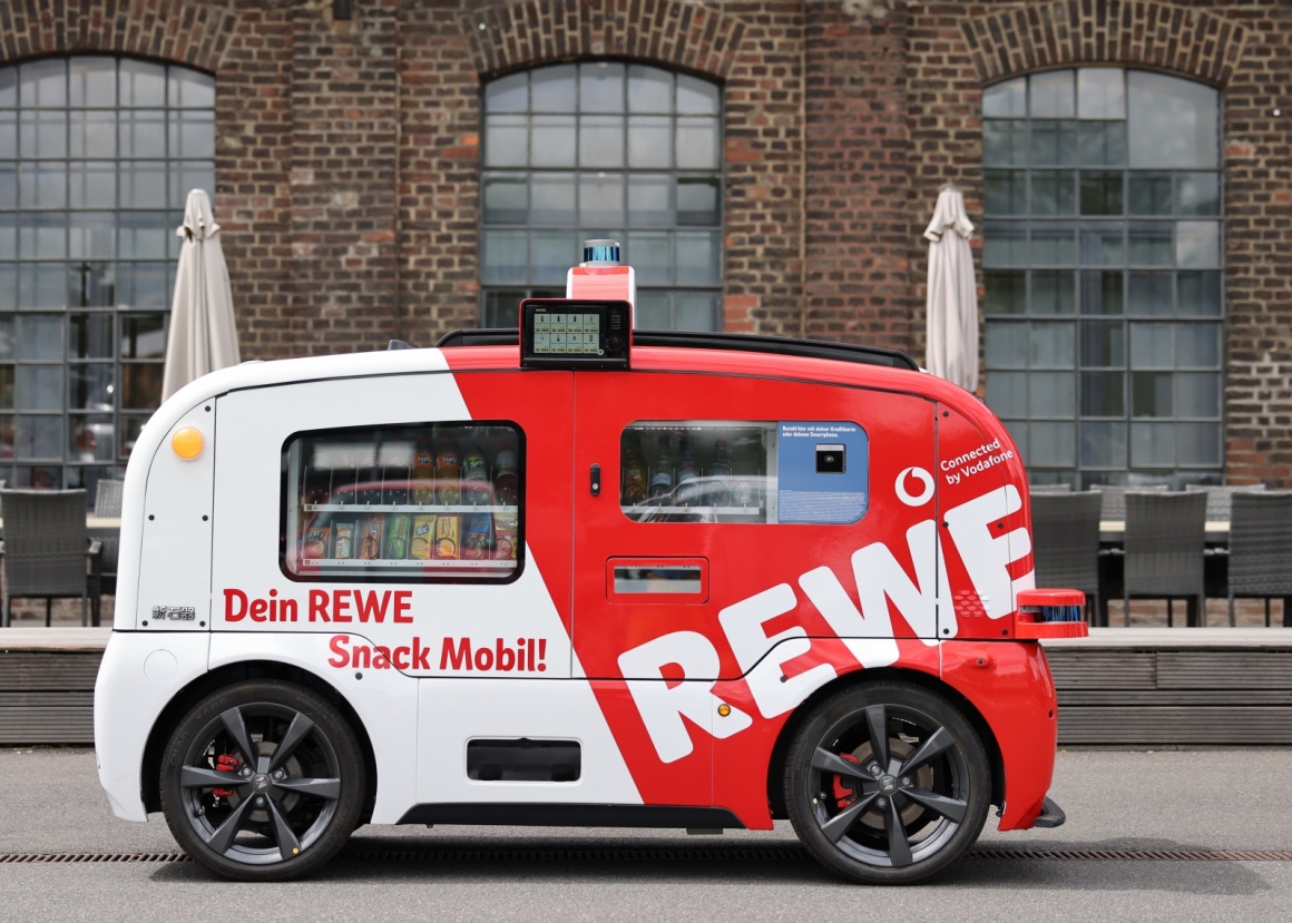 first self-driving kiosk from REWE and Vodafone in front of an old brick...