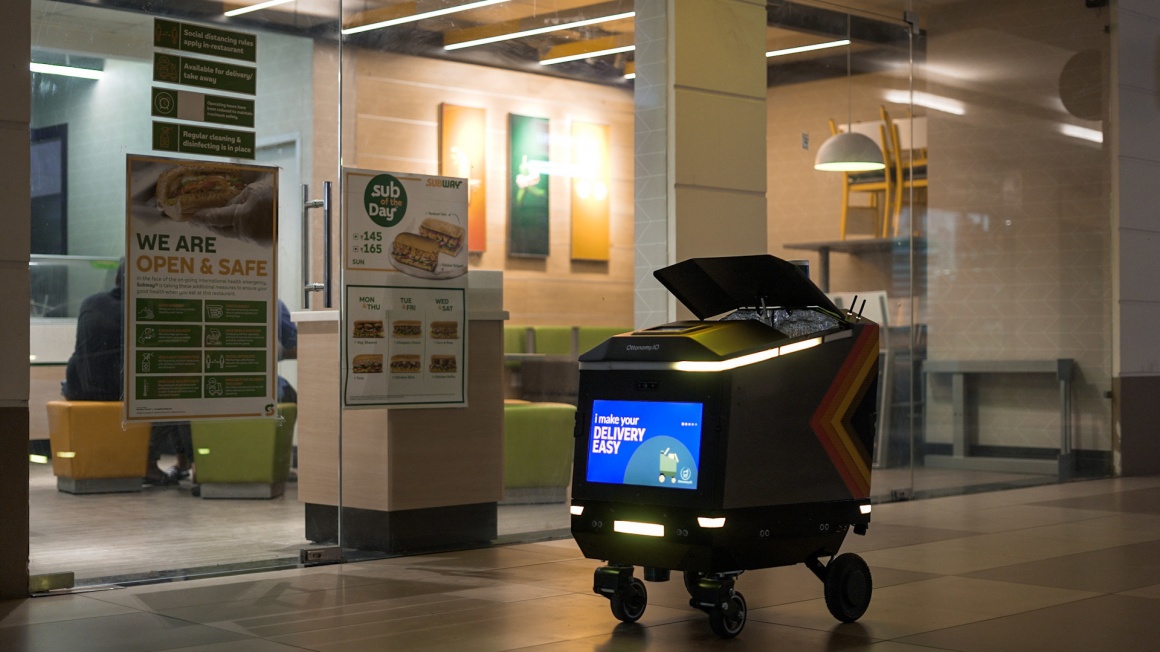 An autonomous delivery robot driving on the street with its open on the top...