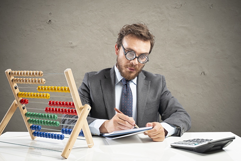 An accountant sits in front of a calculator and an abacus with colored balls;...