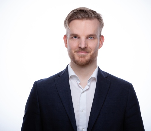 Young blond man wearing a suit smiles at camera