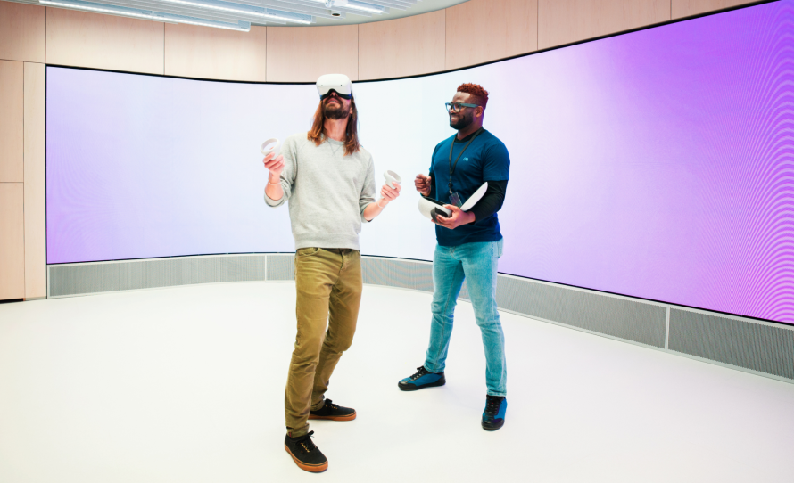 Two people in a VR room, one wearing VR glasses