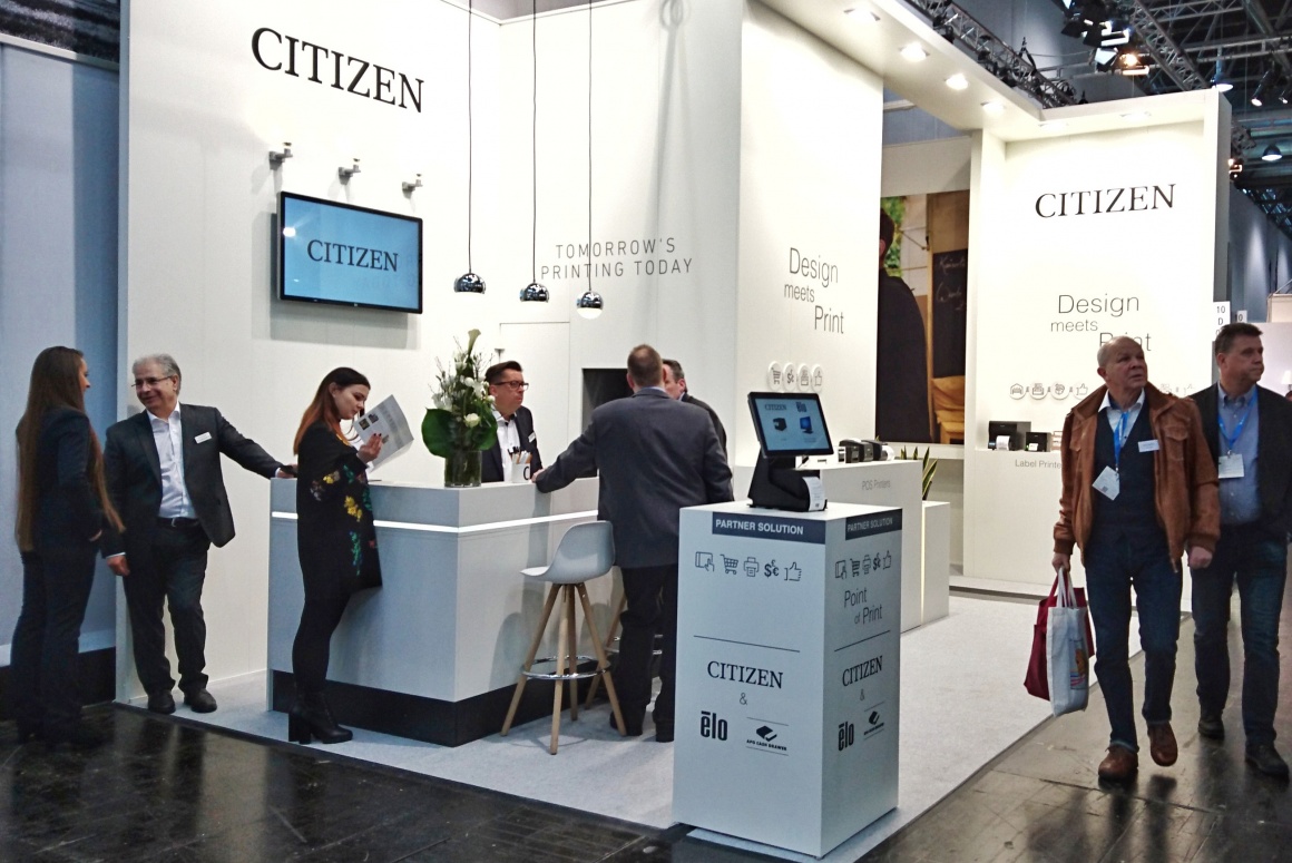 A group of people stands around a booth of Citizen