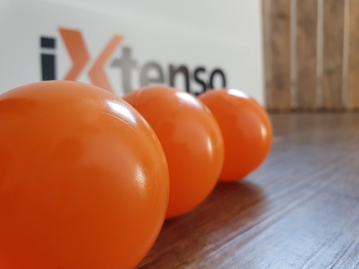 Three orange-red balls in front of an iXtenso sign