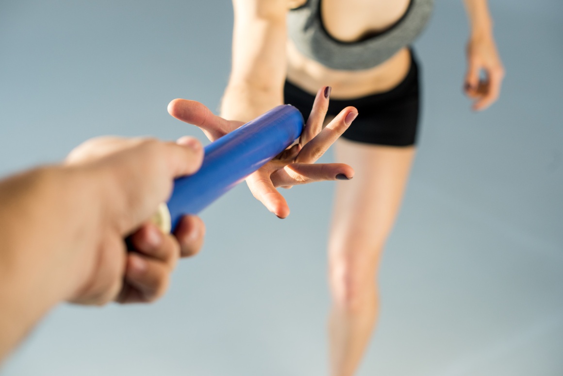 One person takes over a blue baton from another person...