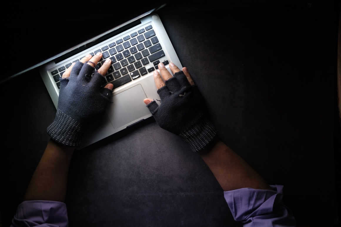 A person using a laptop in the dark while wearing fingerless gloves....