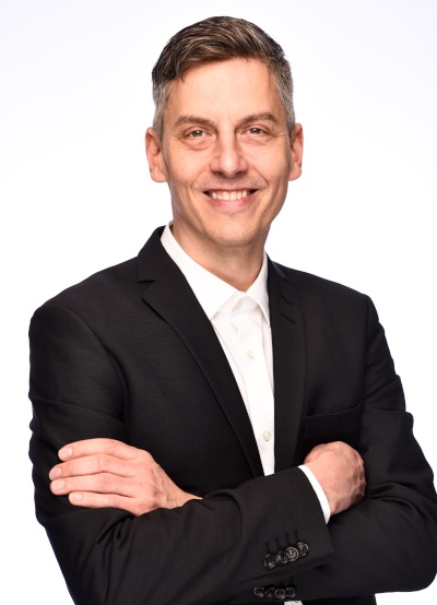 A man in a suit with folded arms smiles at the camera...