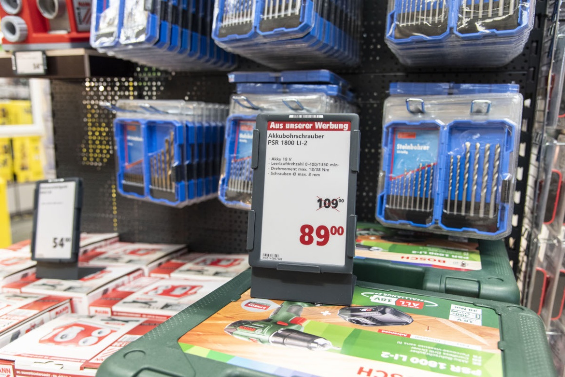 An electronic price tag in front of a shelf with drills in a hardware store;...