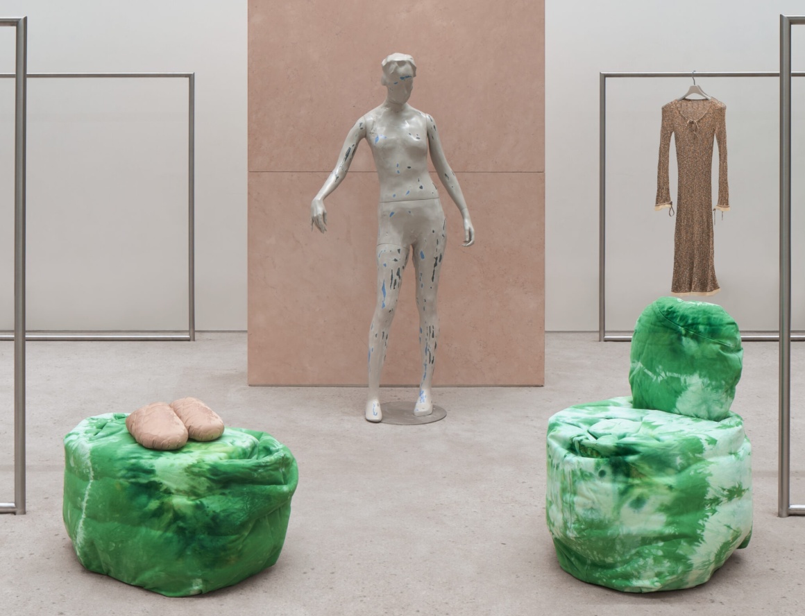 A fashion mannequin stands behind two green lounge chairs...