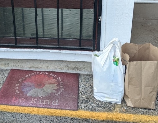 The front porch of an apartment with a welcome mat saying Be Kind and two bags...