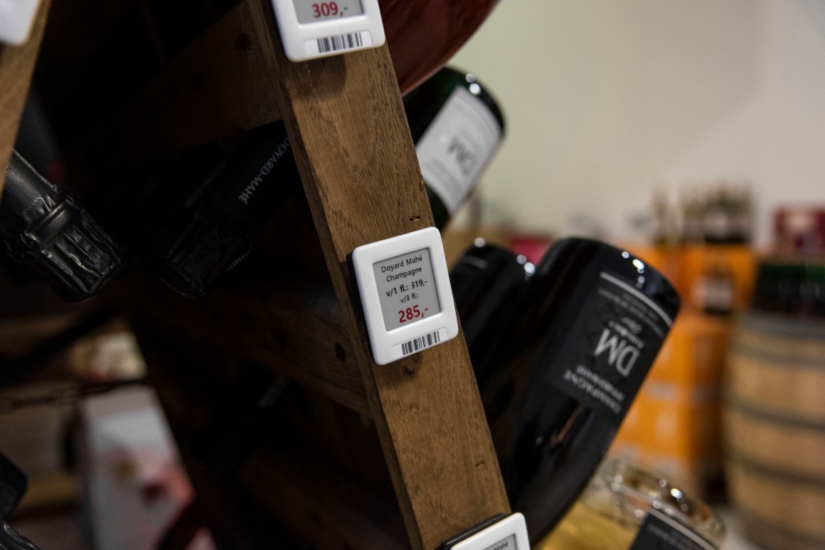 Wine bottles are stuck in a wine rack. Electronic shelf labels are attached to...
