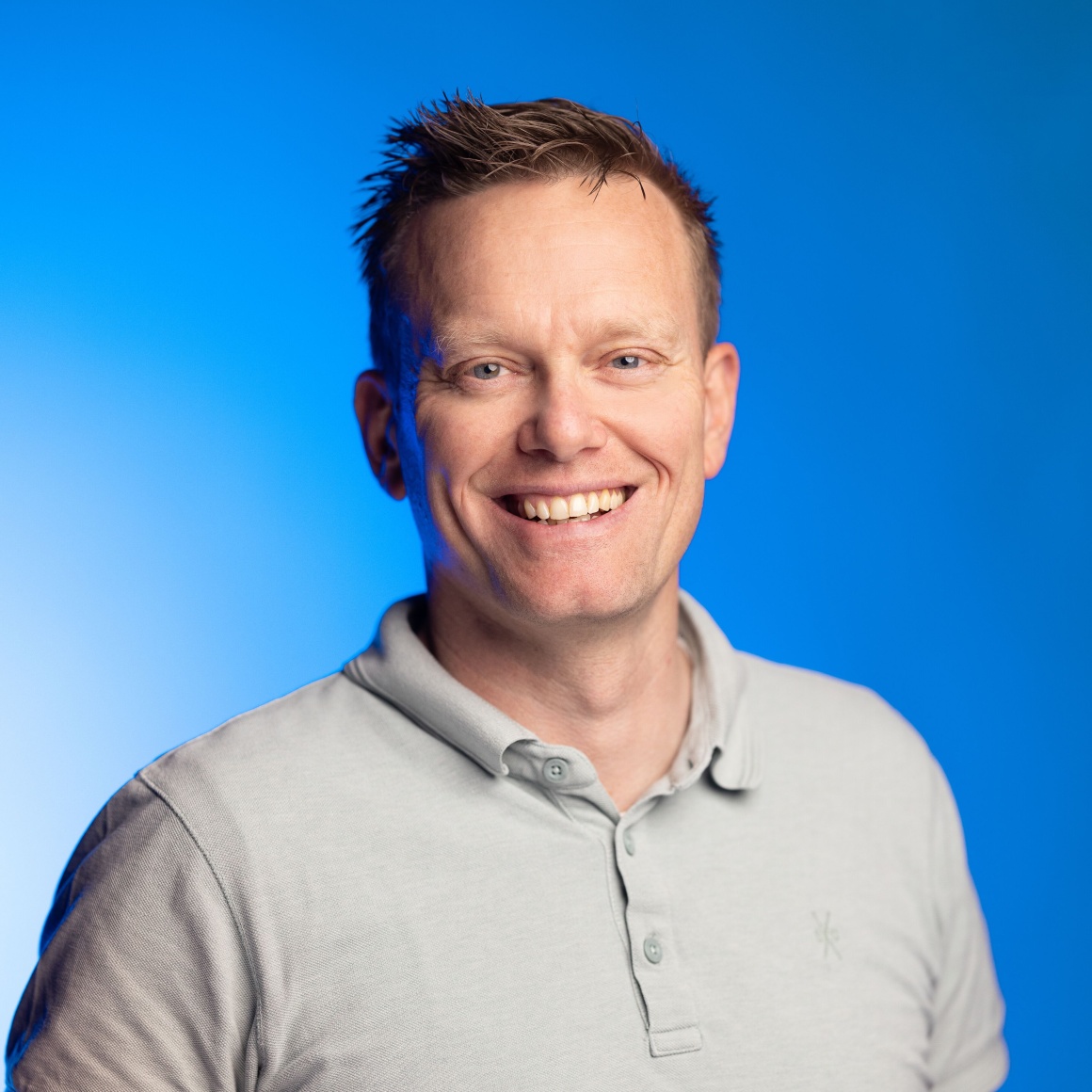 A man with short hair and a grey shirt smiles at the camera...