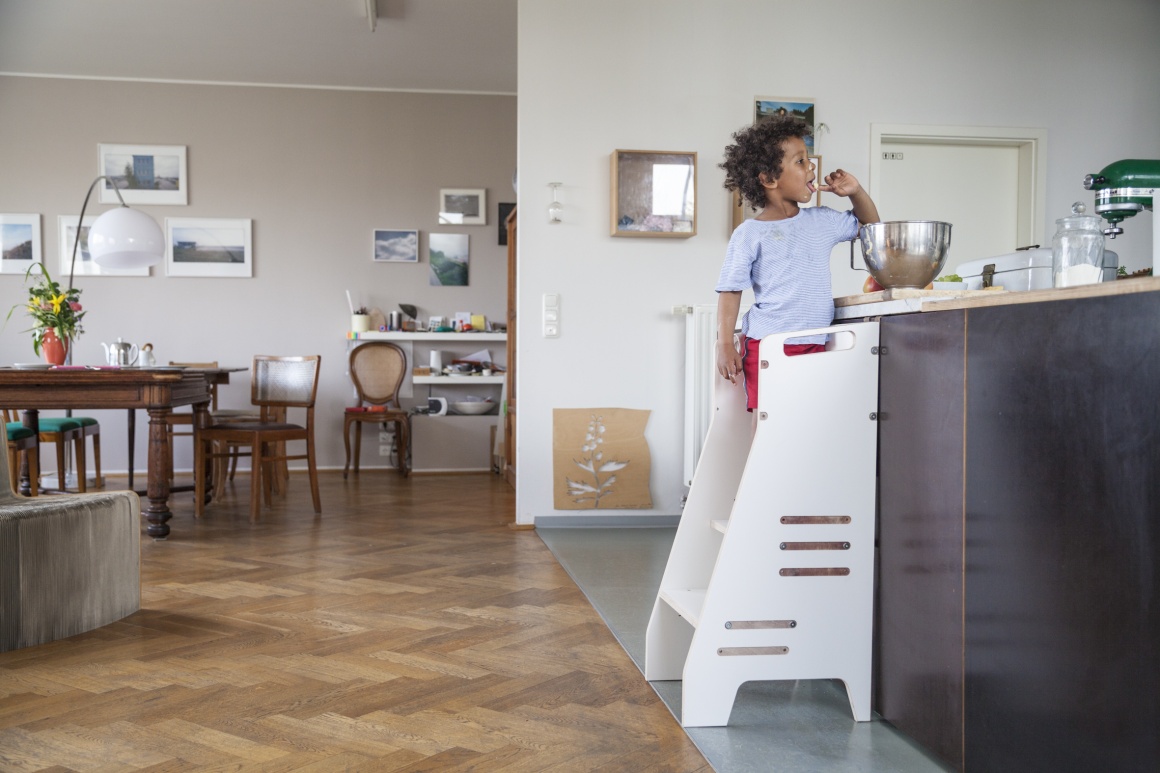 Child standing on a high chair in the kitchen eating dough from a bowl...