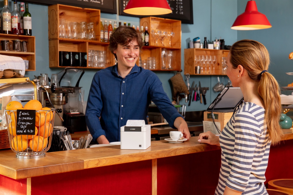 Two people talking at a counter with a POS printer on it...