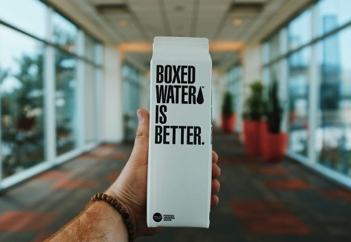 A hand holds a beverage carton with the slogan Boxed Water is better...